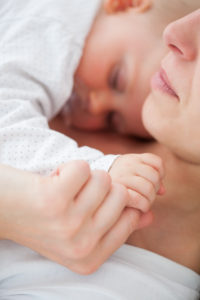 Peaceful woman lying with her baby who is sucking a pacifier indoors