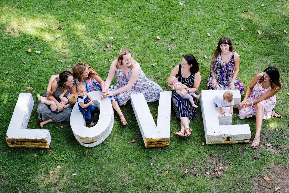 Moms and babies on the grass around giant white letters spelling LOVE