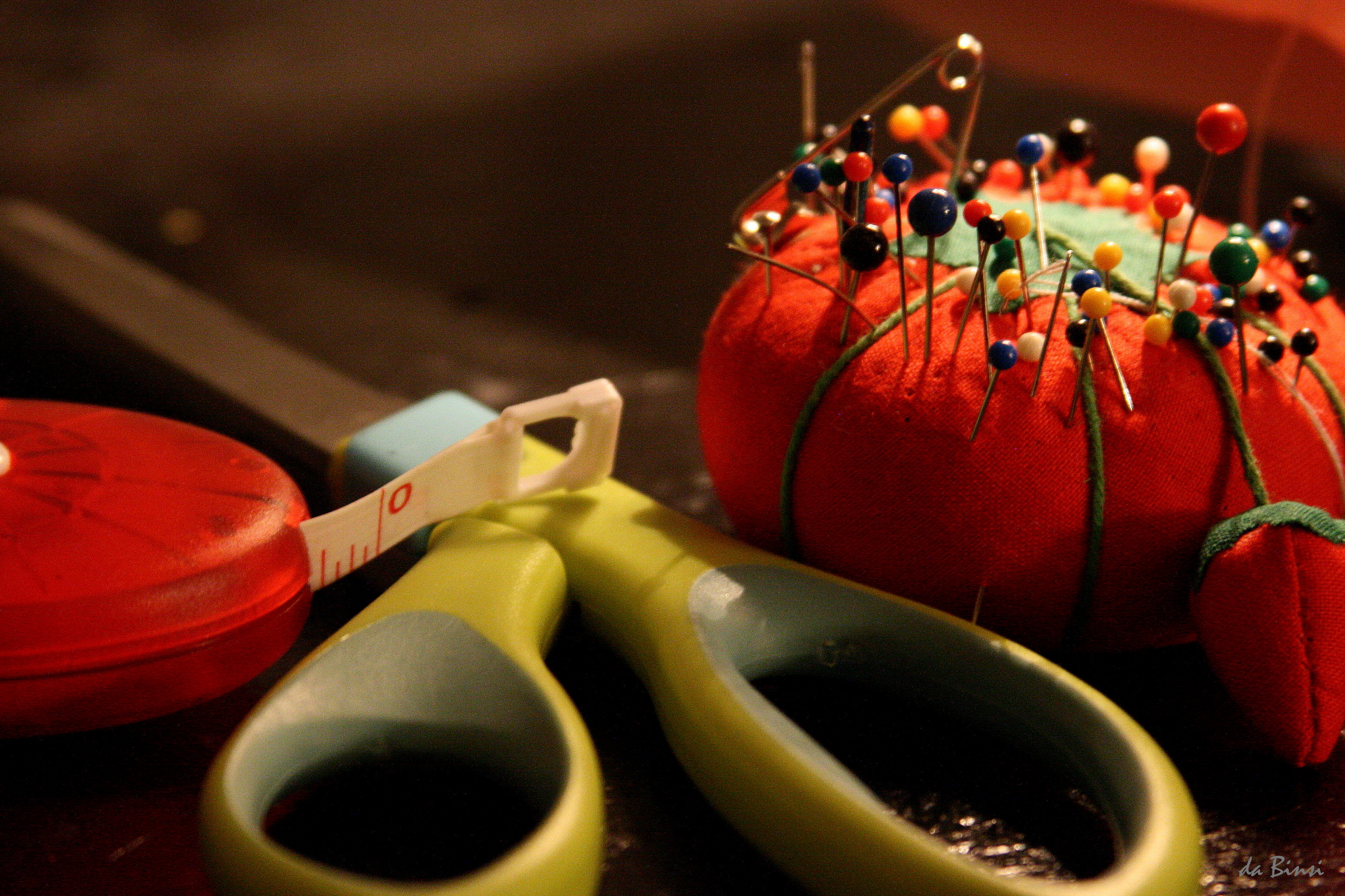Sewing supplies: a red pincushion bristling with pins, green scissors and a tape measure