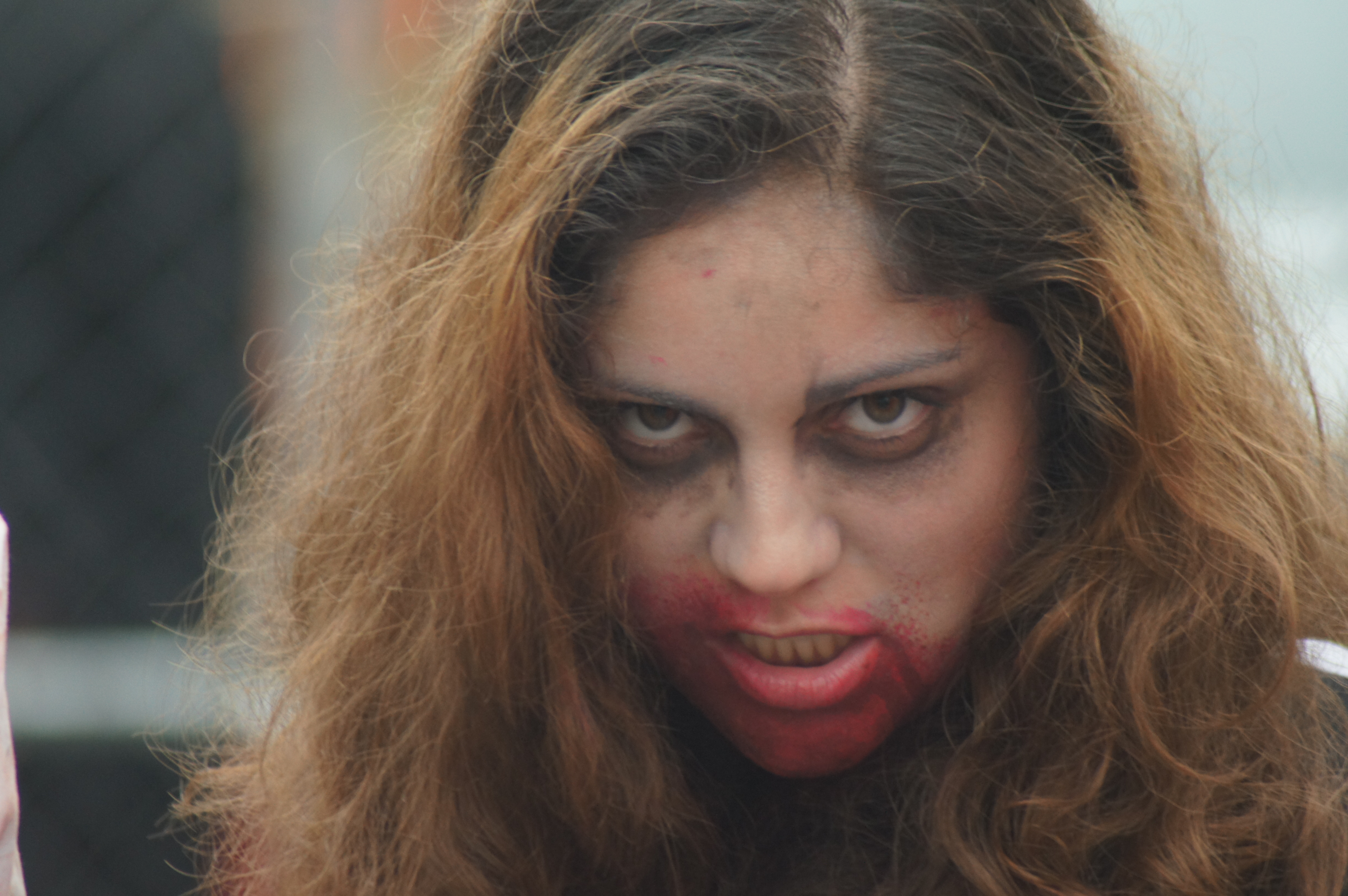 Woman in zombie makeup with dark-ringed eyes and smeared red lips glaring at the camera
