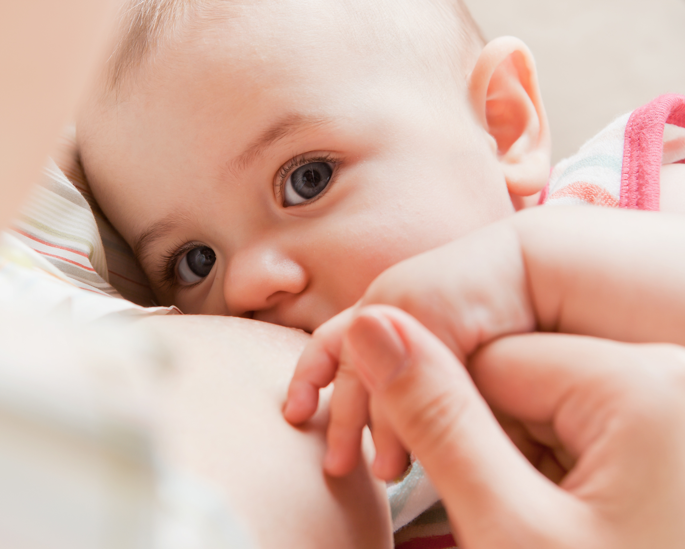 Close-up of a baby breastfeeding and gazing up while gripping mom's finger