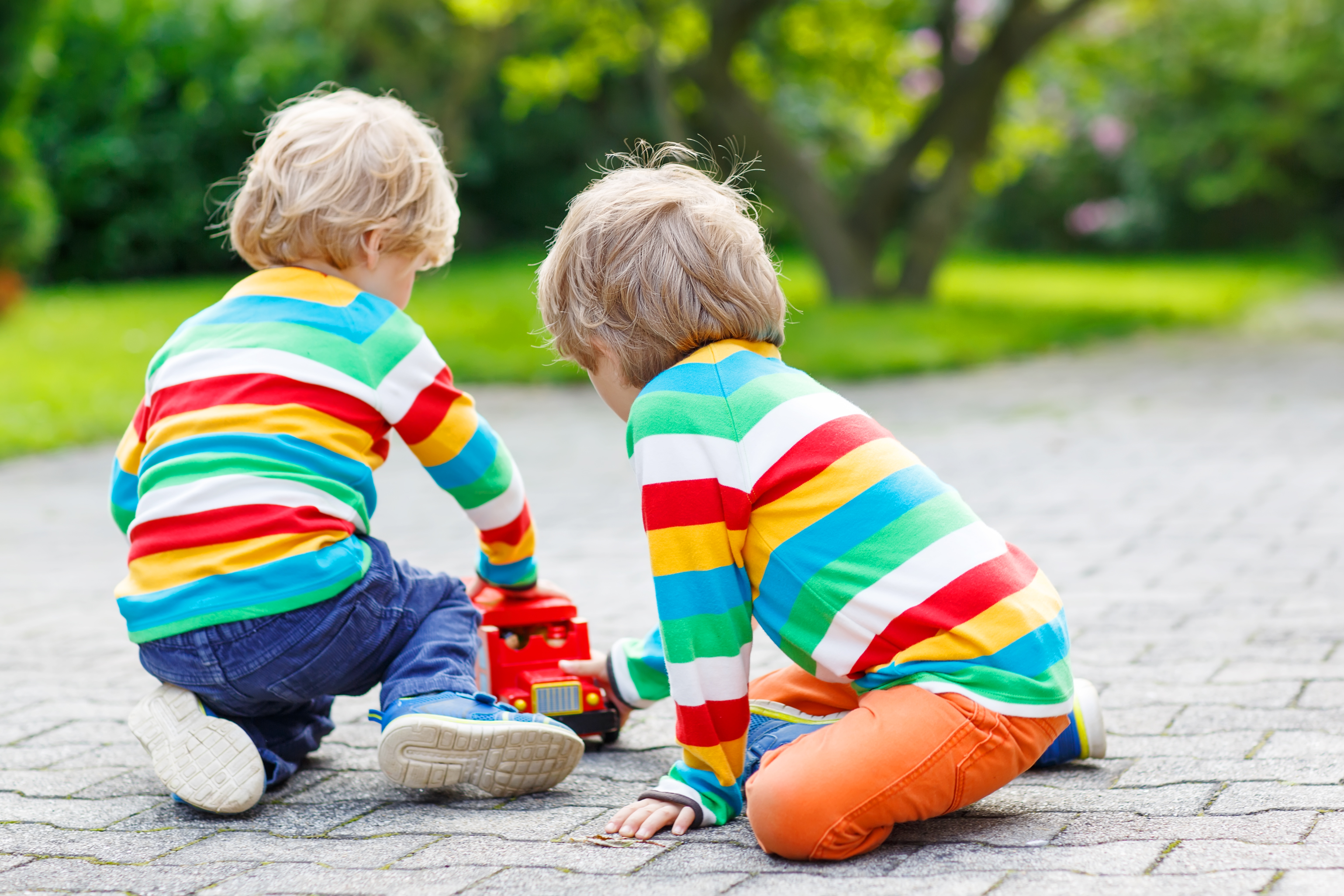 Two young children in matching striped sweaters playing with a toy fire truck on a sidewalk