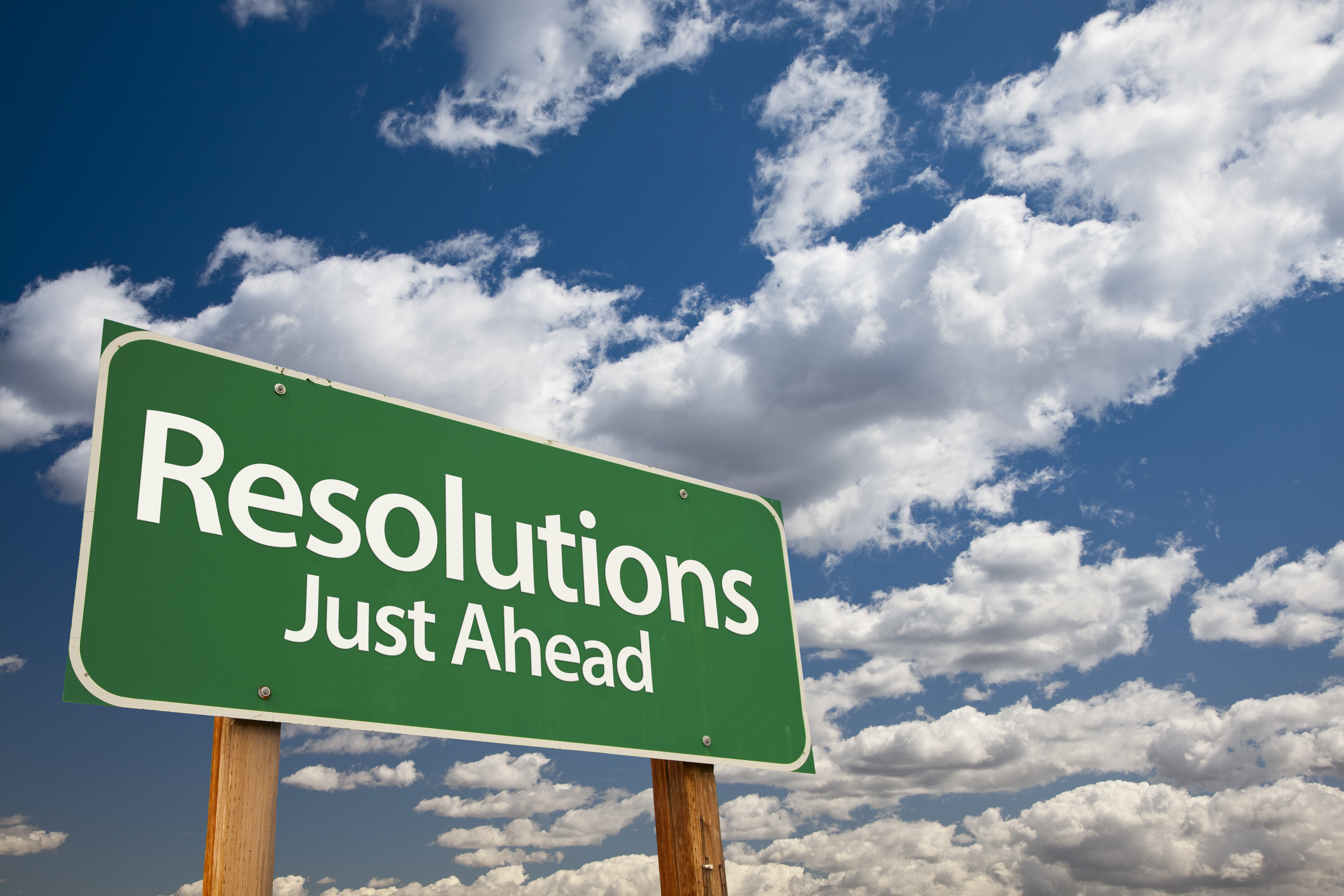 Green road sign reading "Resolutions Just Ahead" against a cloudy blue sky