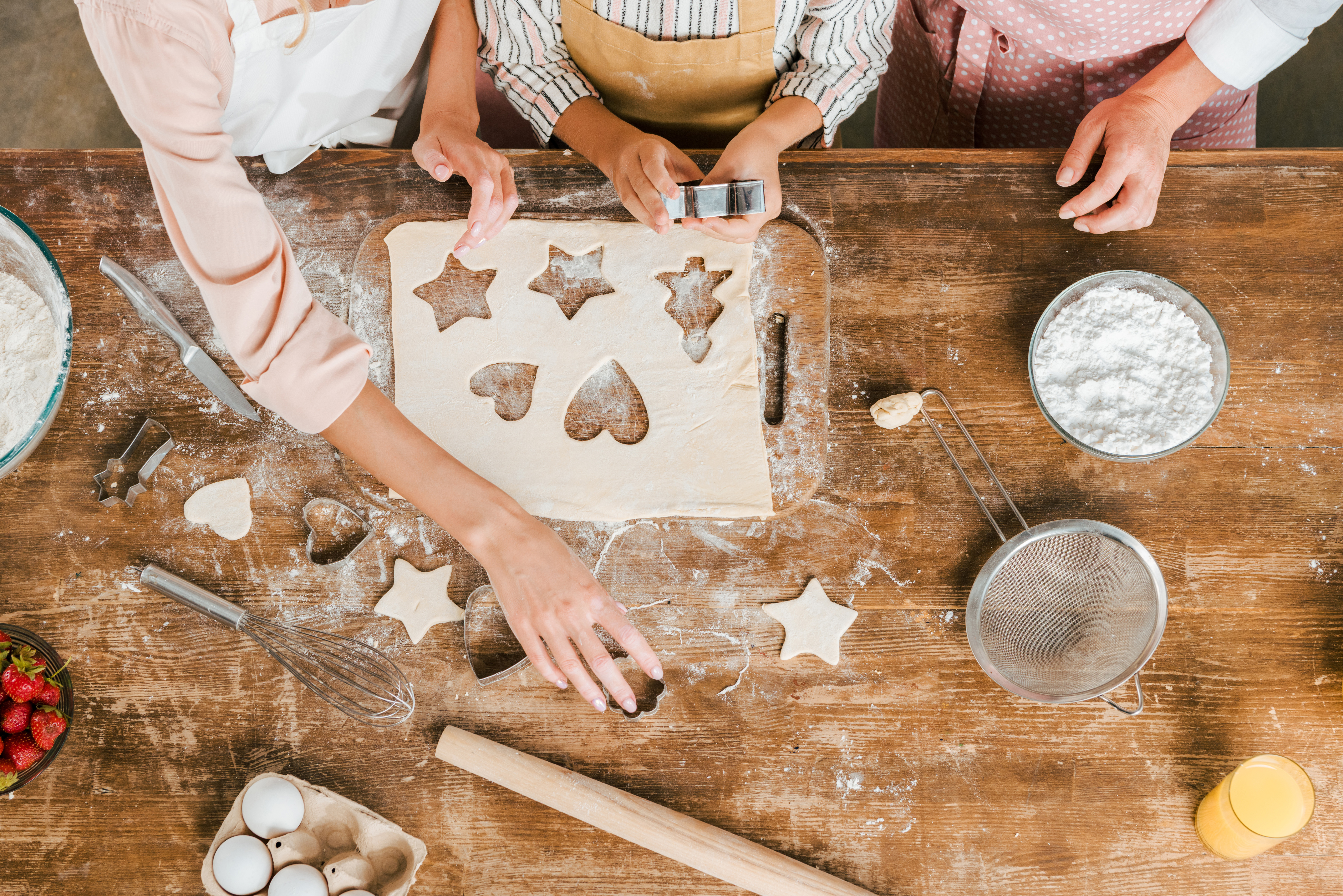 Overhead view of family hands cutting star and heart cookies from rolled dough