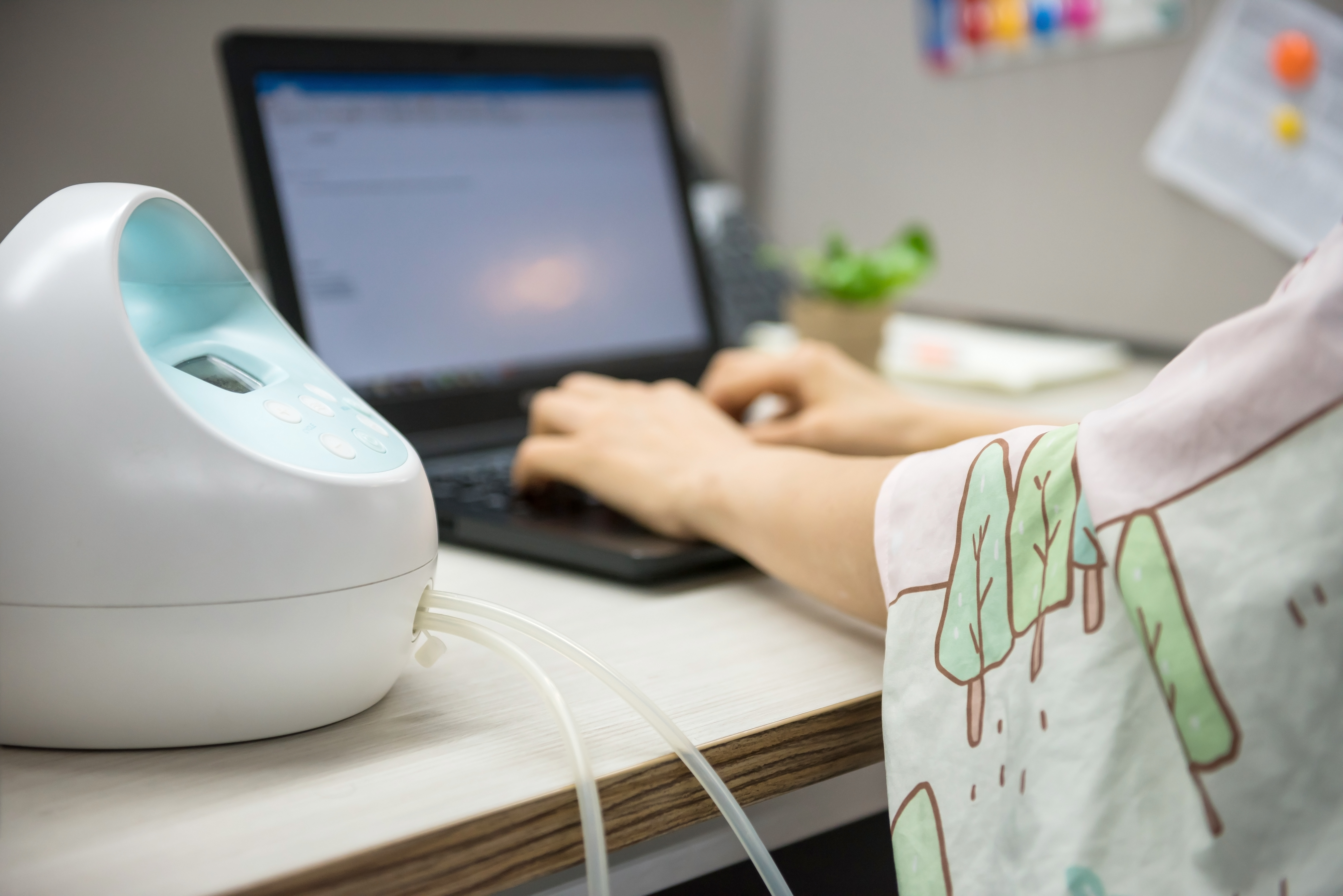 Mom typing on a laptop at her office desk while pumping under a nursing cover