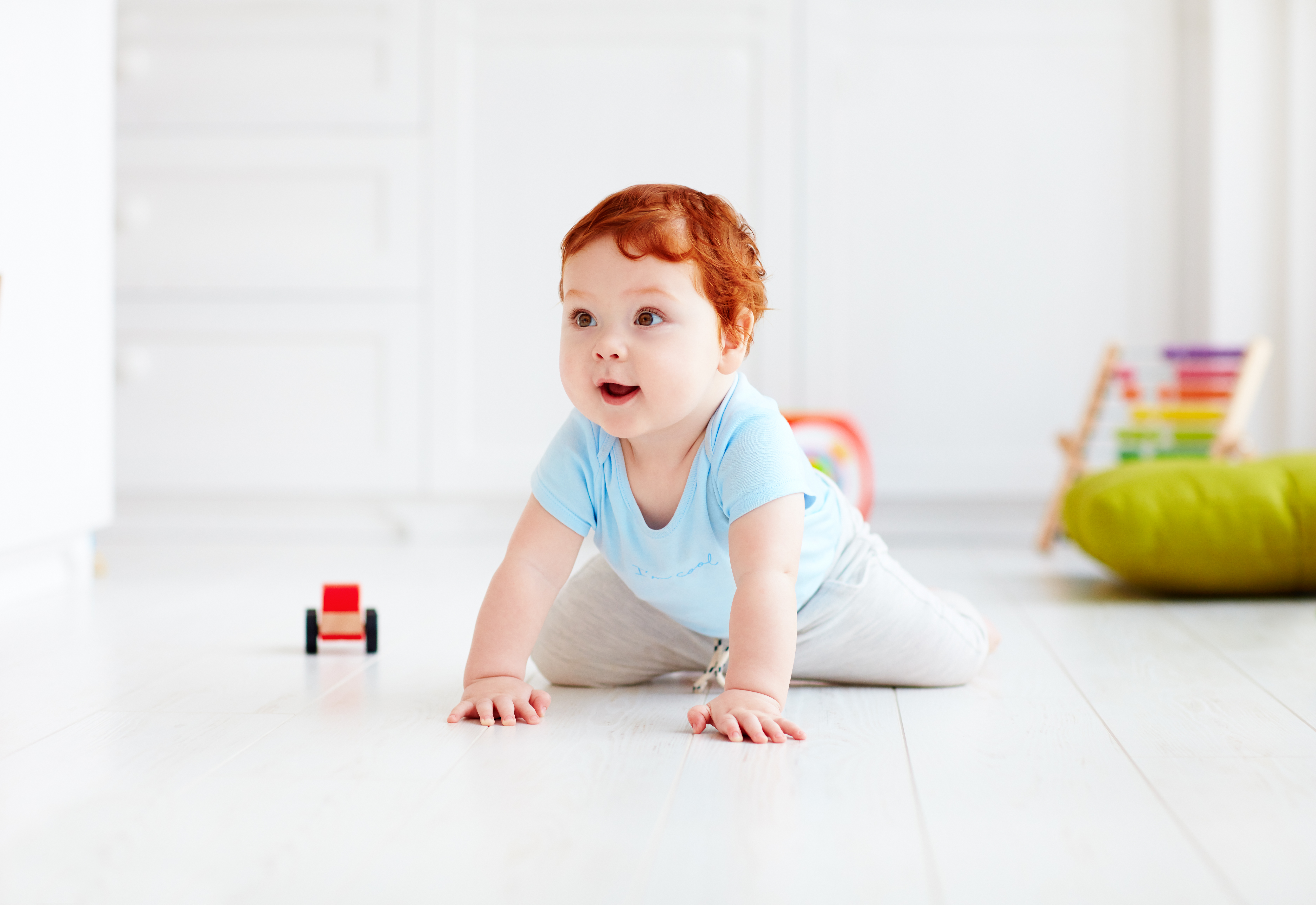 Red-haired baby in a blue shirt crawling across a white floor