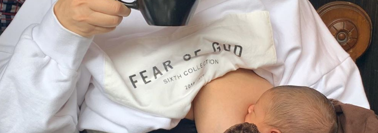 Ashley Graham breastfeeding her newborn son while sipping from a mug
