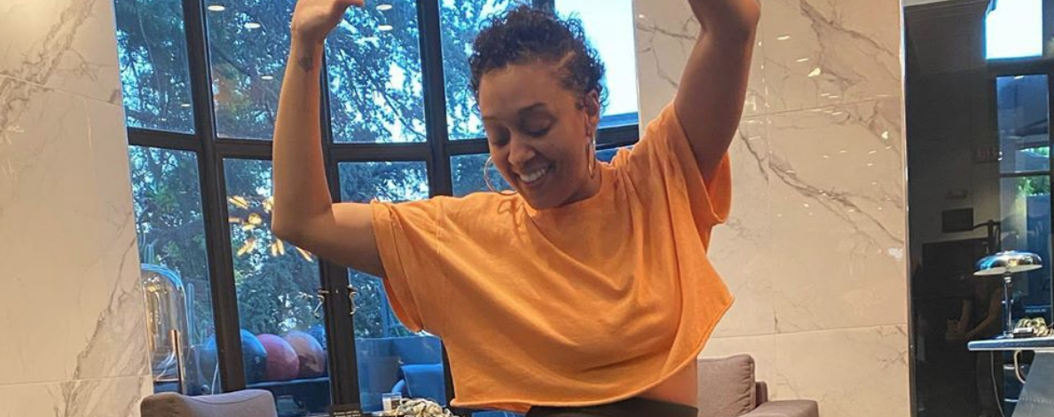 Tia Mowry dancing with her arms raised in an orange crop top