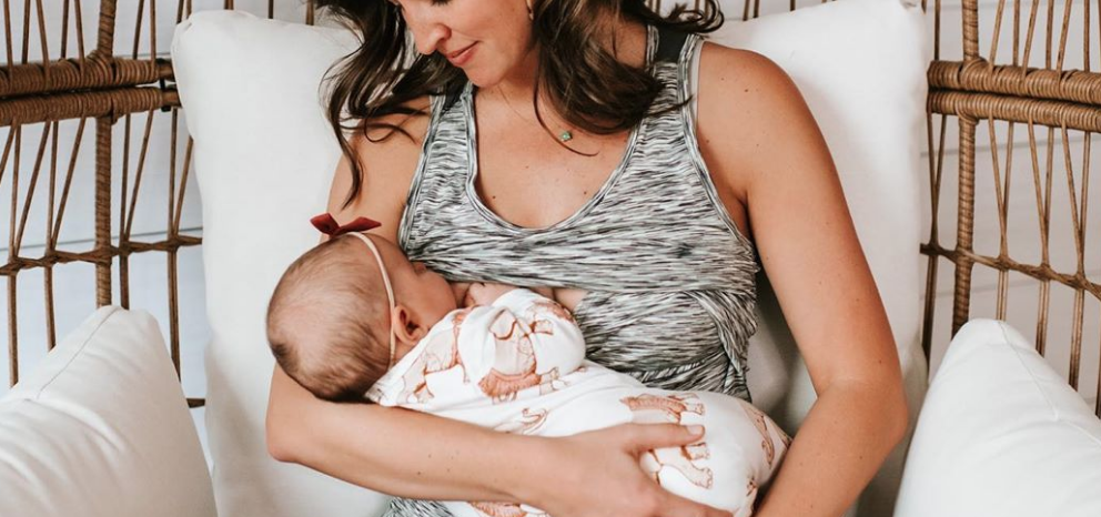 Mom in a wicker chair breastfeeding her baby, who wears a bow headband