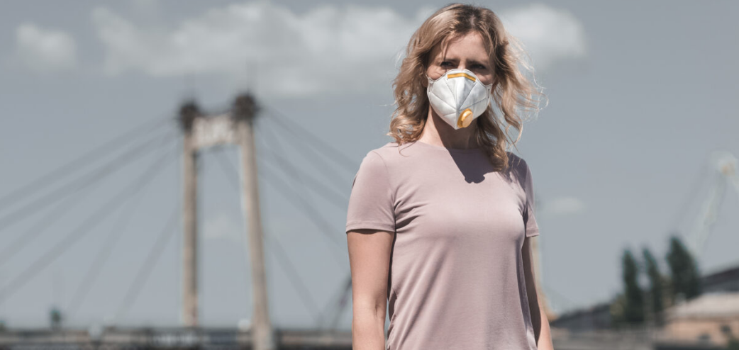 Woman in a protective face mask standing outdoors with a bridge behind her