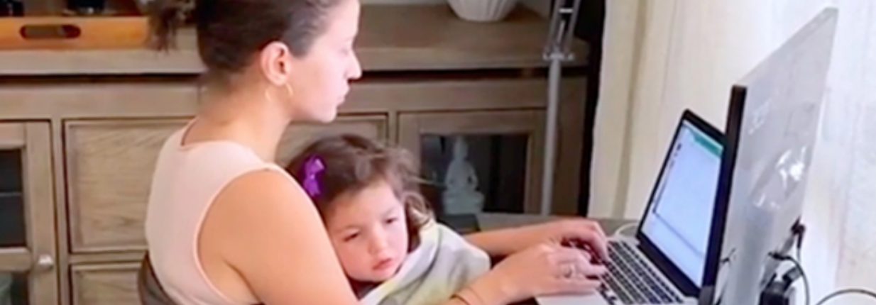 Mom working on a laptop at her desk with her young daughter resting on her lap, from the commercial