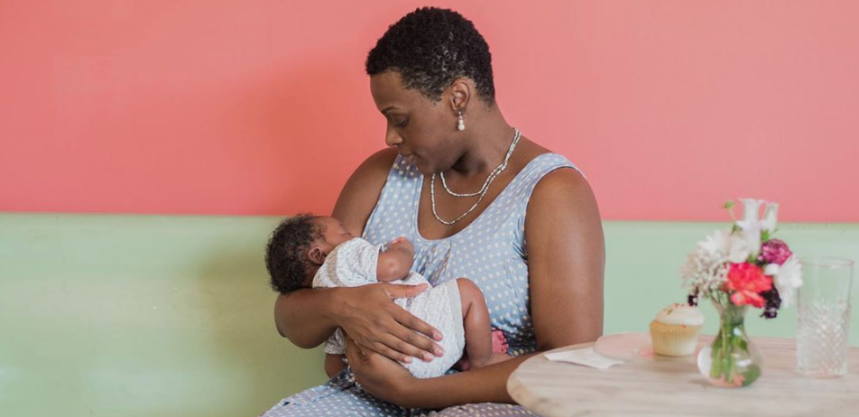 Mother sitting at a café table cradling her sleeping newborn