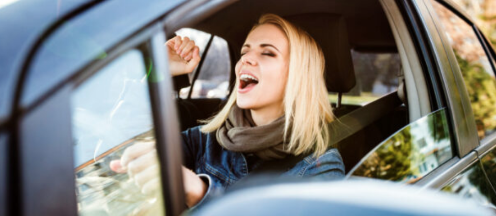 Woman singing loudly with eyes closed and fist raised while driving a car