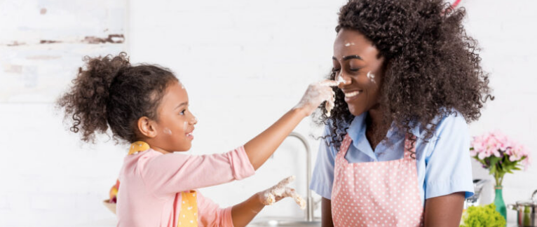 Little girl dabbing flour on her laughing mom's nose as they bake together