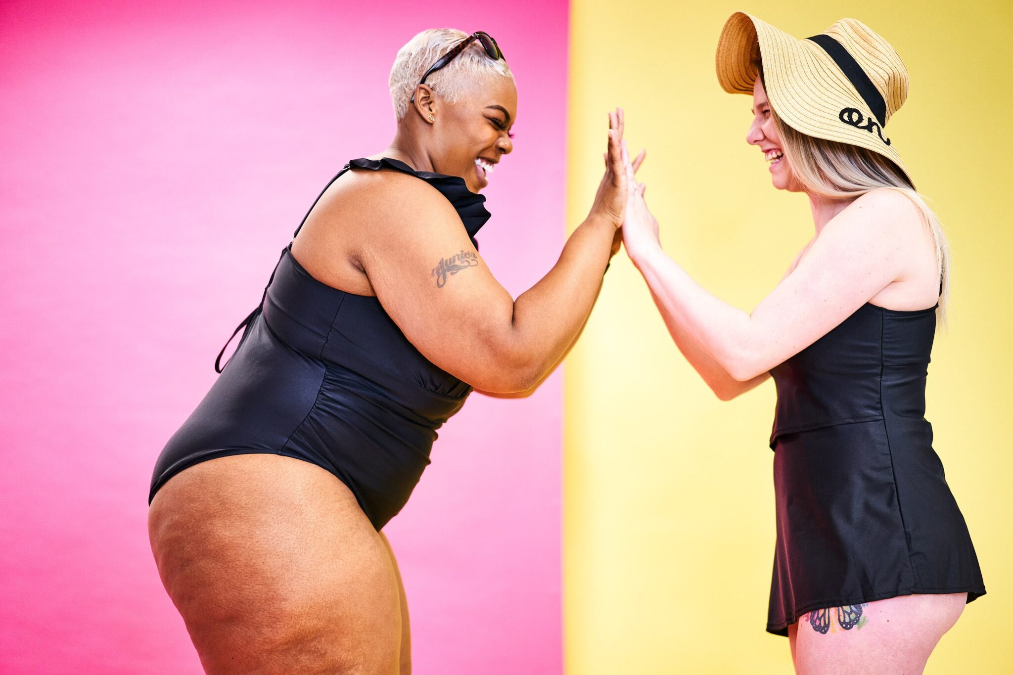 Two laughing women in black swimsuits giving each other a high five